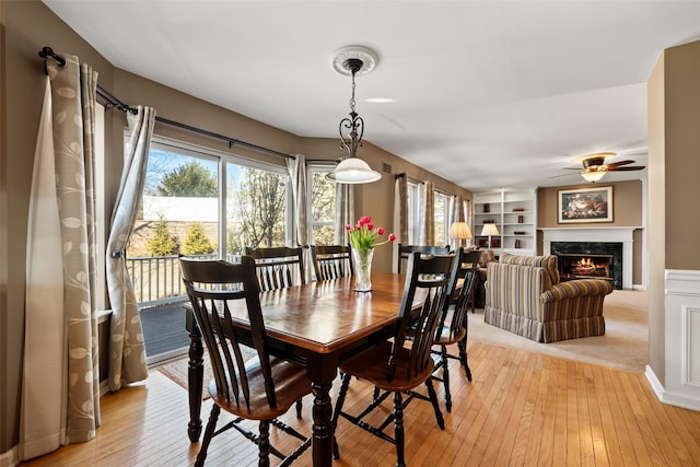 dining space featuring light wood-style flooring, built in shelves, a ceiling fan, and a premium fireplace