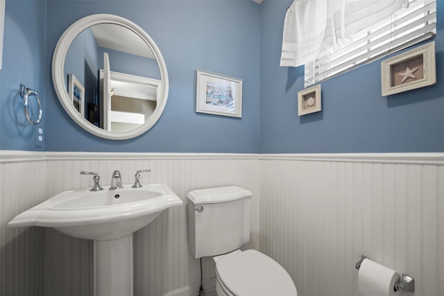 half bathroom with wainscoting, toilet, and a sink