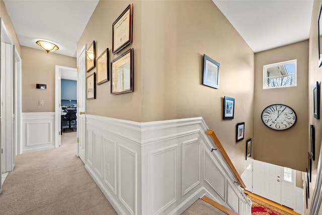 hallway with light carpet, a decorative wall, and wainscoting