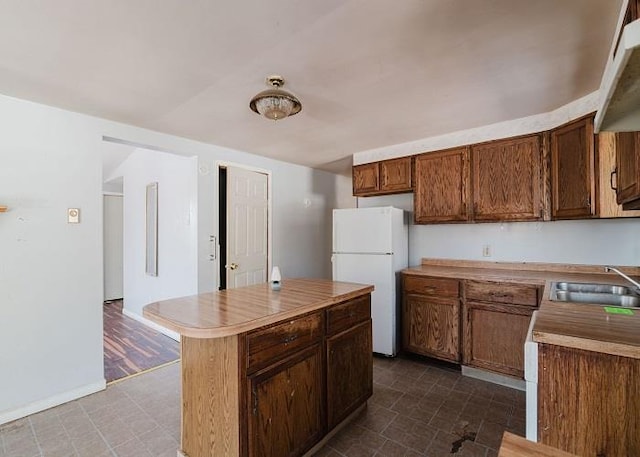 kitchen featuring a kitchen island, light countertops, freestanding refrigerator, brown cabinetry, and a sink