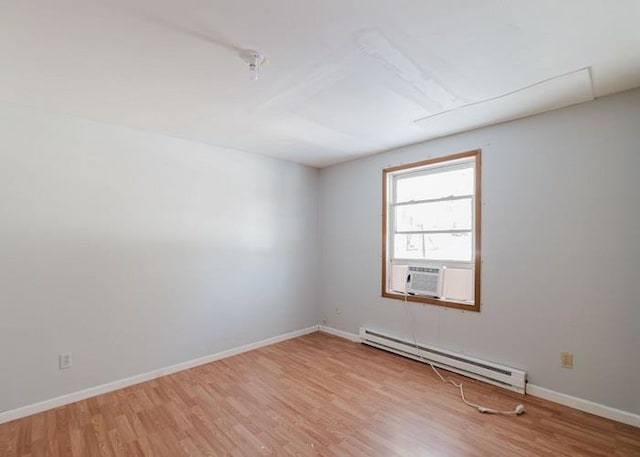 empty room featuring cooling unit, light wood-type flooring, a baseboard heating unit, and baseboards