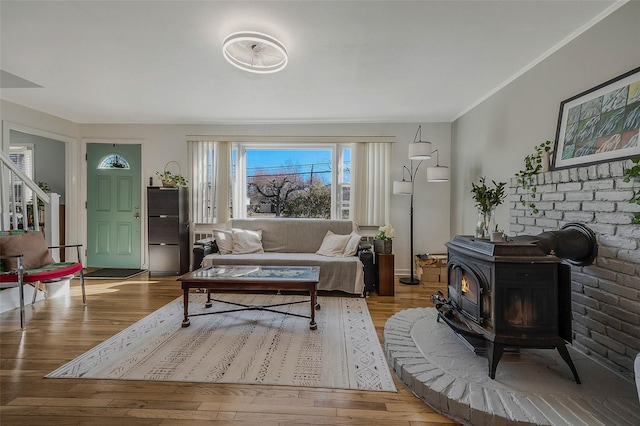 living room featuring wood finished floors, a wood stove, and ornamental molding