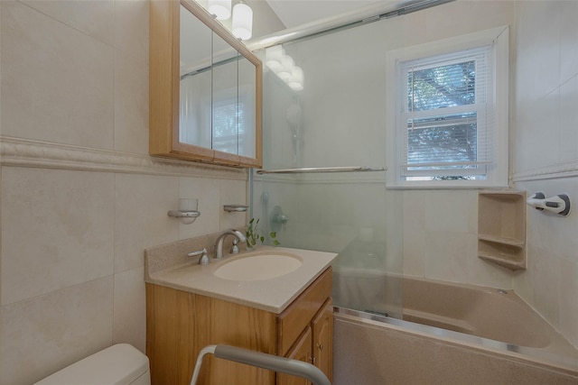 bathroom with toilet, tile walls, vanity, and shower / bath combination with glass door