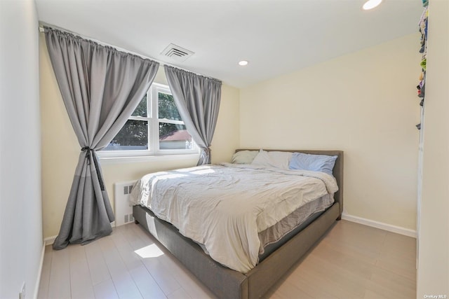 bedroom with radiator, wood finished floors, visible vents, baseboards, and recessed lighting