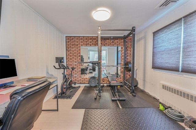 exercise area with radiator heating unit, visible vents, and brick wall