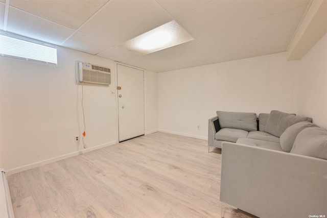 living area with a drop ceiling, baseboards, a wall mounted AC, and light wood-style floors