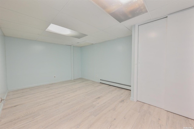 empty room featuring a baseboard heating unit, a paneled ceiling, baseboards, and wood finished floors