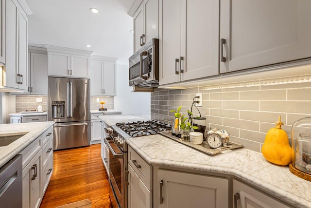 kitchen featuring decorative backsplash, light wood finished floors, light stone countertops, and appliances with stainless steel finishes