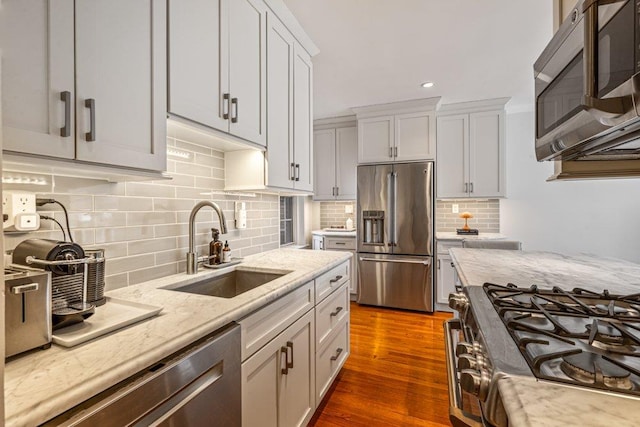 kitchen featuring a sink, light stone counters, dark wood finished floors, appliances with stainless steel finishes, and decorative backsplash