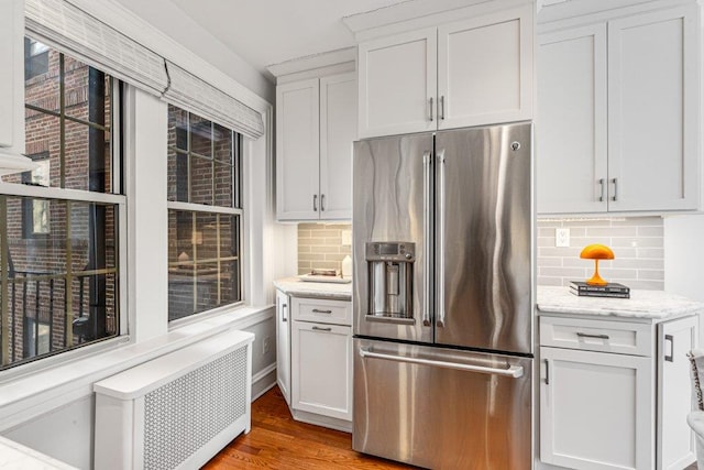 kitchen featuring radiator, light wood-type flooring, white cabinets, high end refrigerator, and tasteful backsplash