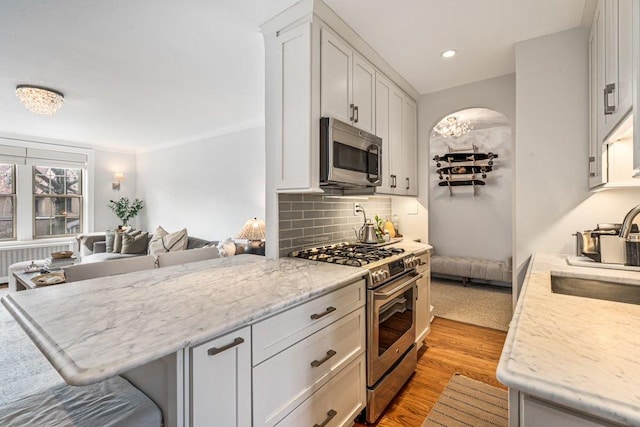 kitchen featuring light wood-type flooring, light stone counters, backsplash, white cabinetry, and stainless steel appliances