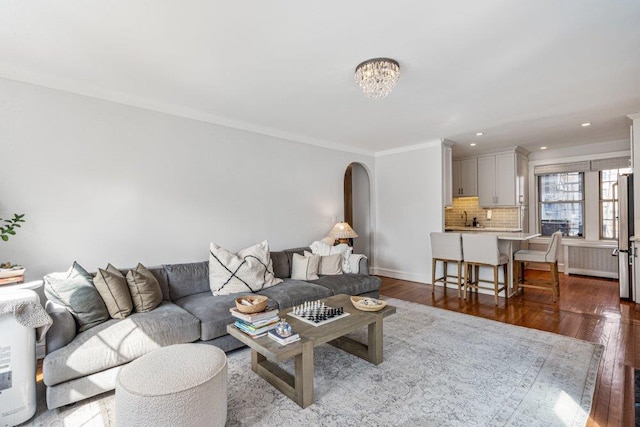 living room featuring baseboards, arched walkways, dark wood-type flooring, and crown molding