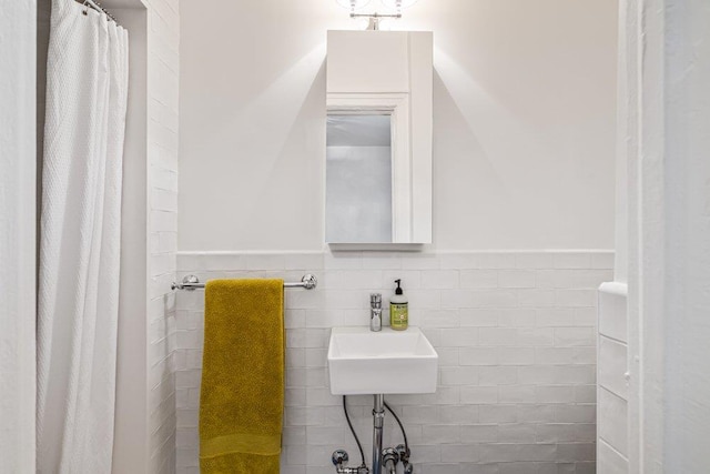 bathroom featuring a sink, tile walls, a shower with curtain, and wainscoting