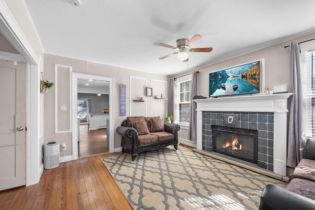 living area featuring baseboard heating, a healthy amount of sunlight, a tile fireplace, and hardwood / wood-style flooring