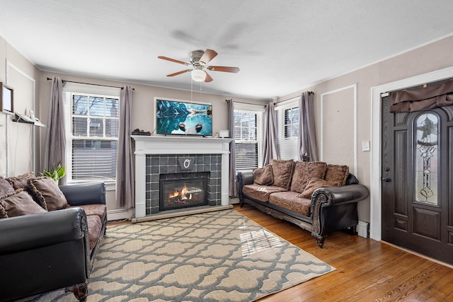 living room featuring a ceiling fan, baseboard heating, a tile fireplace, and hardwood / wood-style flooring