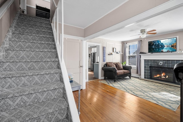 stairway featuring wood-type flooring, a ceiling fan, ornamental molding, and a tiled fireplace