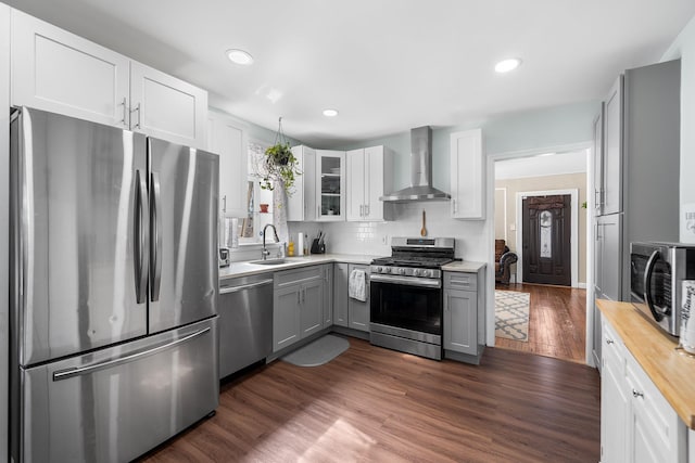 kitchen with butcher block counters, appliances with stainless steel finishes, dark wood-style floors, wall chimney exhaust hood, and a sink