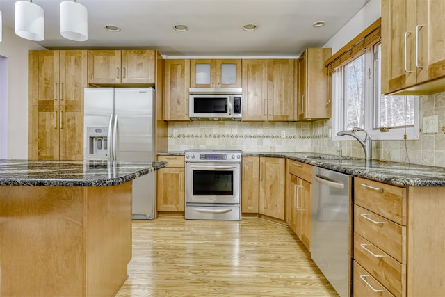 kitchen featuring dark stone countertops, a sink, decorative backsplash, light wood-style floors, and appliances with stainless steel finishes