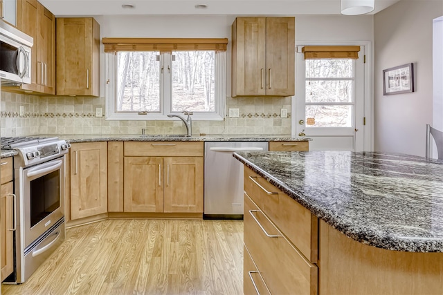 kitchen featuring dark stone counters, light wood-style flooring, a sink, decorative backsplash, and stainless steel appliances