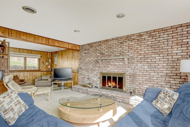 living room with visible vents, brick wall, wood walls, a brick fireplace, and carpet flooring