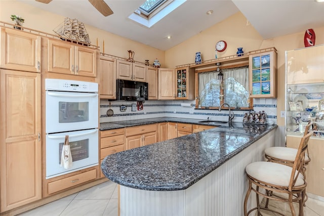 kitchen with black appliances, a breakfast bar, light brown cabinets, a peninsula, and glass insert cabinets