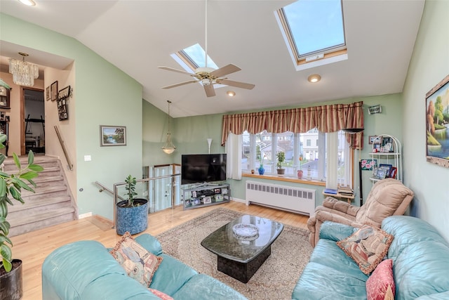 living room featuring stairs, vaulted ceiling with skylight, radiator heating unit, and wood finished floors