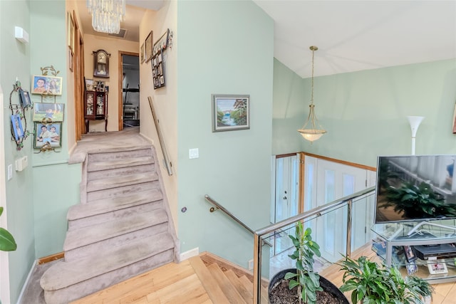 stairway with an inviting chandelier, wood finished floors, baseboards, and vaulted ceiling