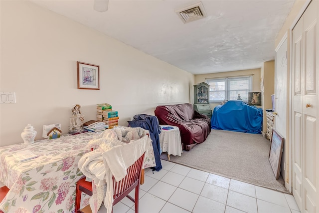 bedroom with light tile patterned floors, light colored carpet, visible vents, and a closet