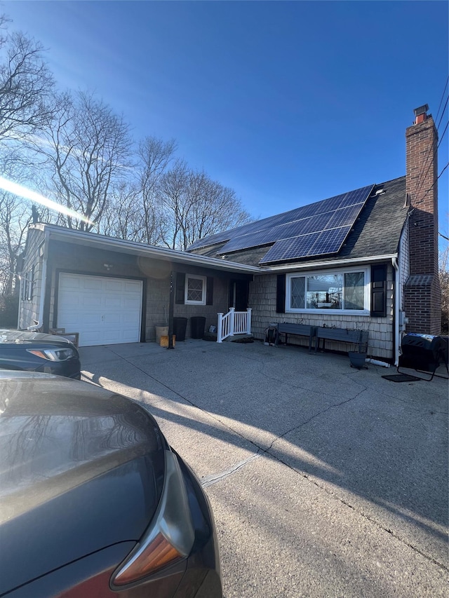 single story home featuring roof with shingles, solar panels, a chimney, concrete driveway, and a garage