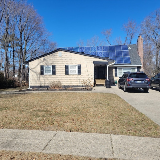 ranch-style home with a front lawn, concrete driveway, roof with shingles, roof mounted solar panels, and a chimney