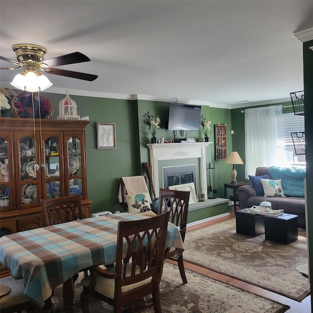 dining room featuring ceiling fan, wood finished floors, a glass covered fireplace, and crown molding