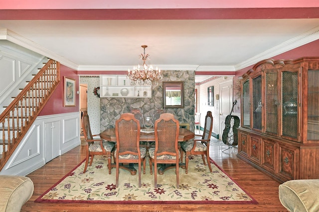 dining room with wood finished floors, a wainscoted wall, stairs, crown molding, and a chandelier