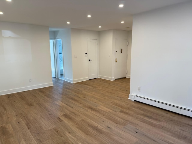 spare room featuring recessed lighting, a baseboard heating unit, baseboards, and wood finished floors