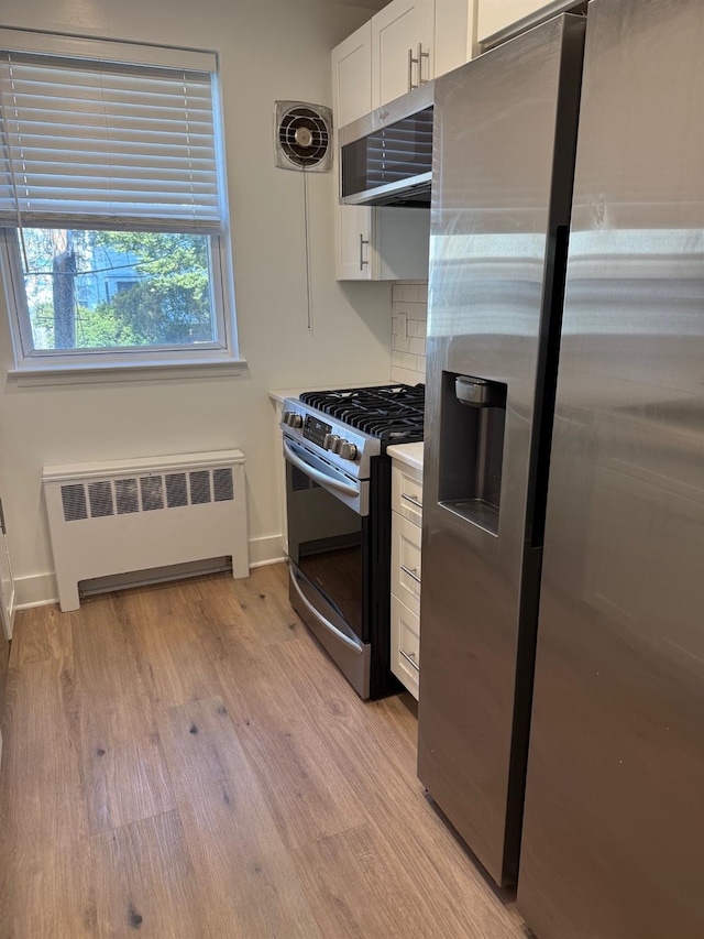 kitchen with visible vents, radiator heating unit, stainless steel appliances, white cabinets, and light wood-type flooring