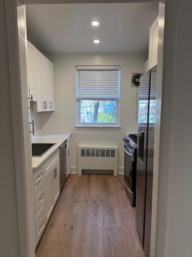 kitchen with tasteful backsplash, radiator, appliances with stainless steel finishes, wood finished floors, and a sink