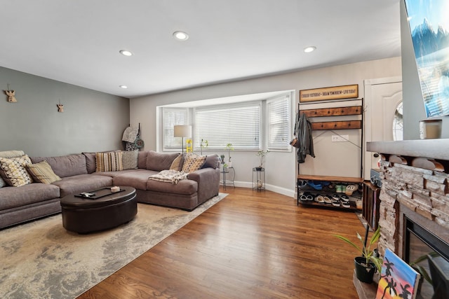 living area featuring recessed lighting, baseboards, a stone fireplace, and wood finished floors