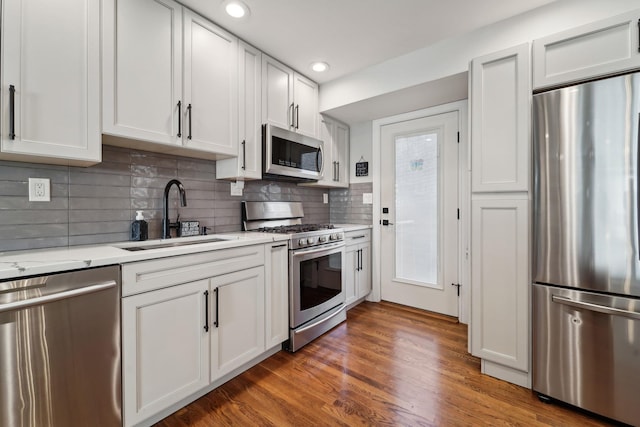 kitchen featuring a sink, light stone counters, backsplash, wood finished floors, and stainless steel appliances