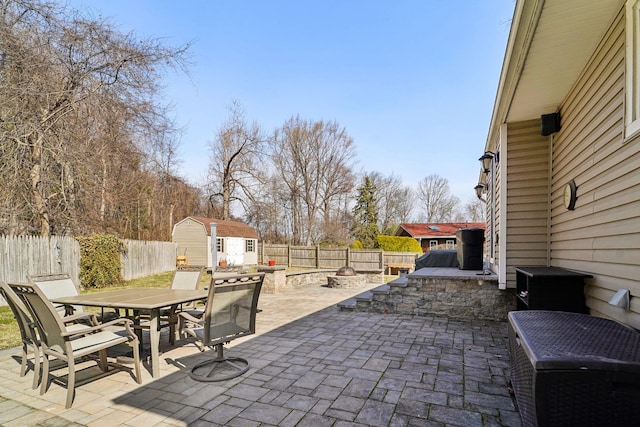 view of patio / terrace with a fire pit, outdoor dining area, a fenced backyard, an outbuilding, and a storage unit