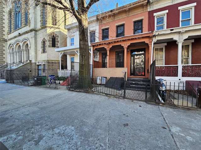 view of front facade featuring covered porch, fence, and brick siding