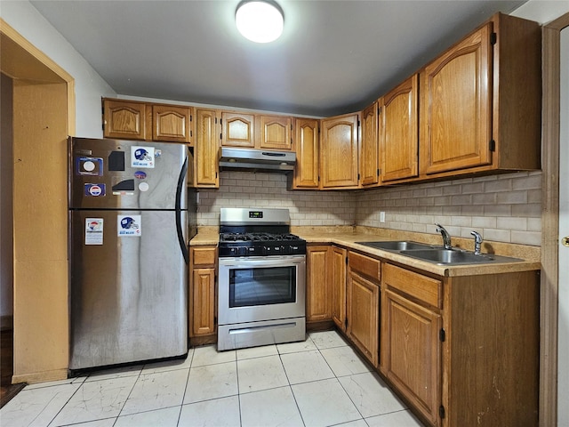 kitchen featuring under cabinet range hood, brown cabinets, appliances with stainless steel finishes, and a sink