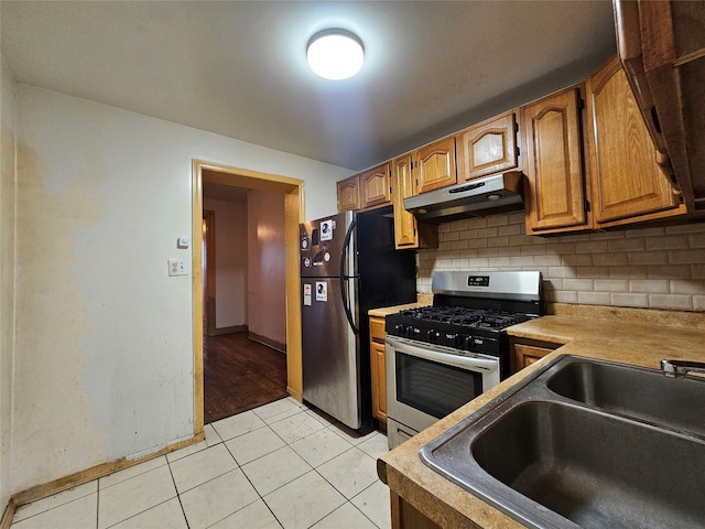 kitchen featuring under cabinet range hood, a sink, stainless steel appliances, light tile patterned flooring, and decorative backsplash