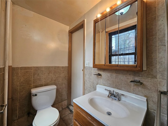 bathroom with toilet, tile walls, wainscoting, and vanity