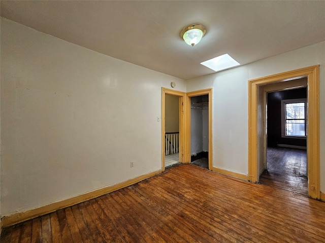 unfurnished bedroom featuring a skylight, a closet, baseboards, and wood-type flooring