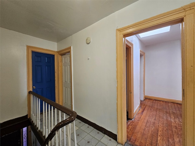 corridor featuring an upstairs landing, baseboards, and light wood finished floors