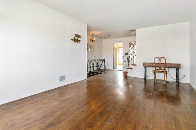 unfurnished room with visible vents, baseboards, stairway, an inviting chandelier, and wood-type flooring