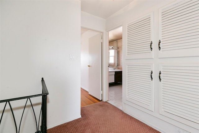 hall with an upstairs landing, carpet flooring, and baseboards