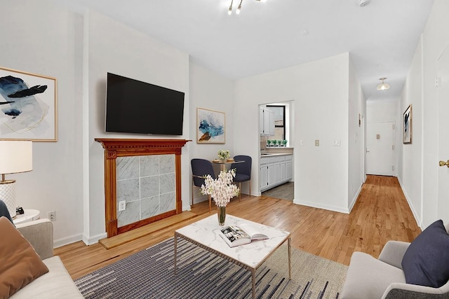 living room featuring baseboards, light wood-style floors, and a tile fireplace