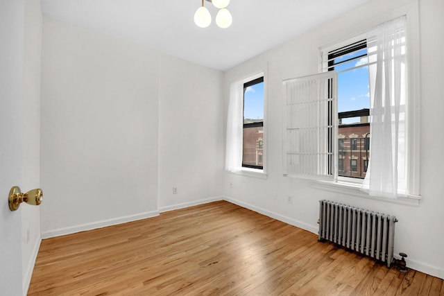 unfurnished room featuring baseboards, an inviting chandelier, radiator heating unit, and light wood finished floors