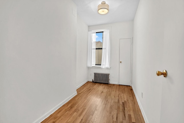 empty room featuring baseboards, radiator heating unit, and light wood-style floors