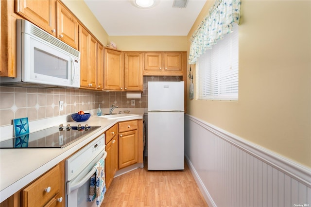 kitchen with white appliances, light wood finished floors, a sink, light countertops, and wainscoting